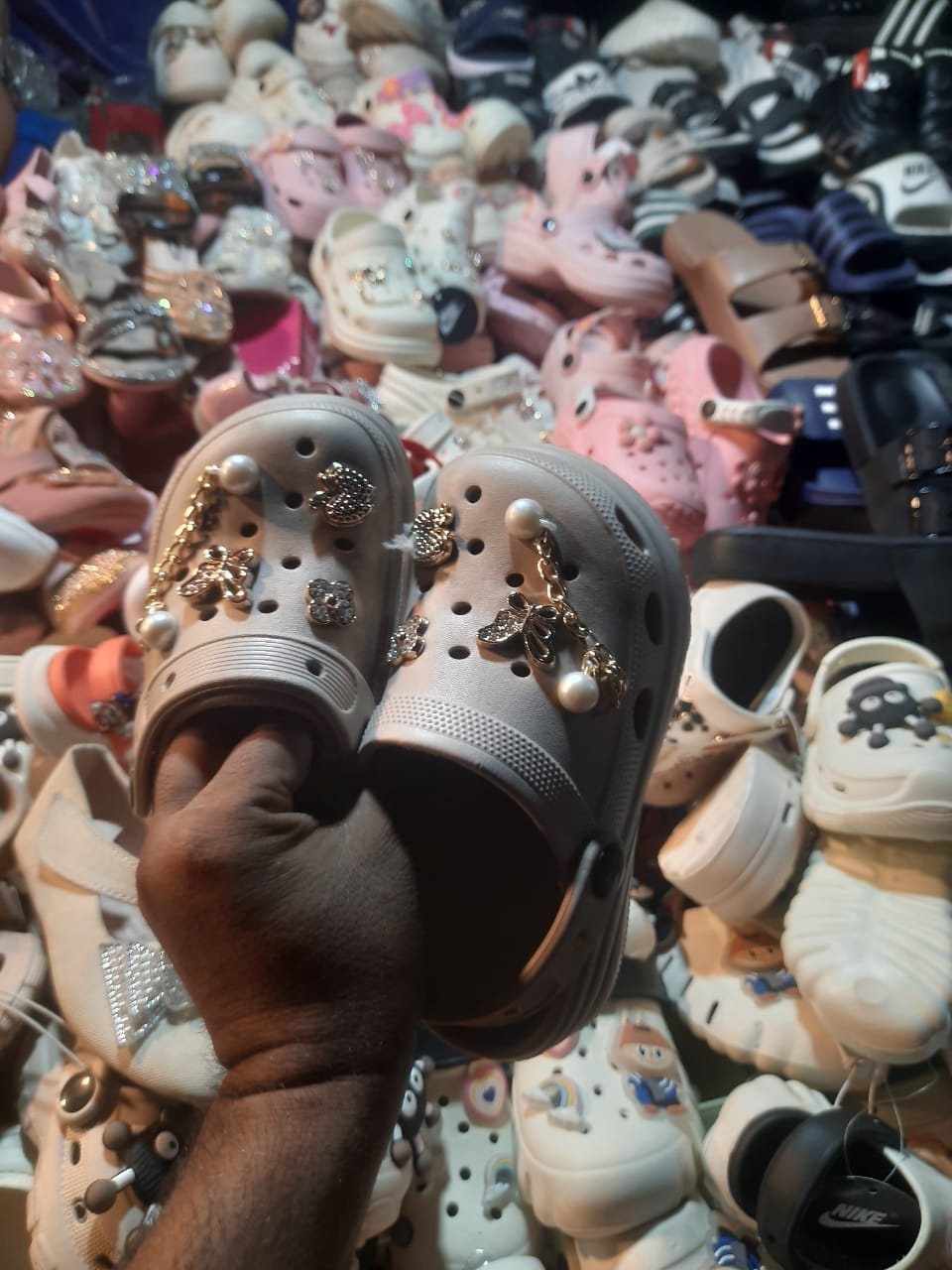 Small clog-style shoes decorated with pearl, chain and gold butterfly charms in front of a pile of clogs